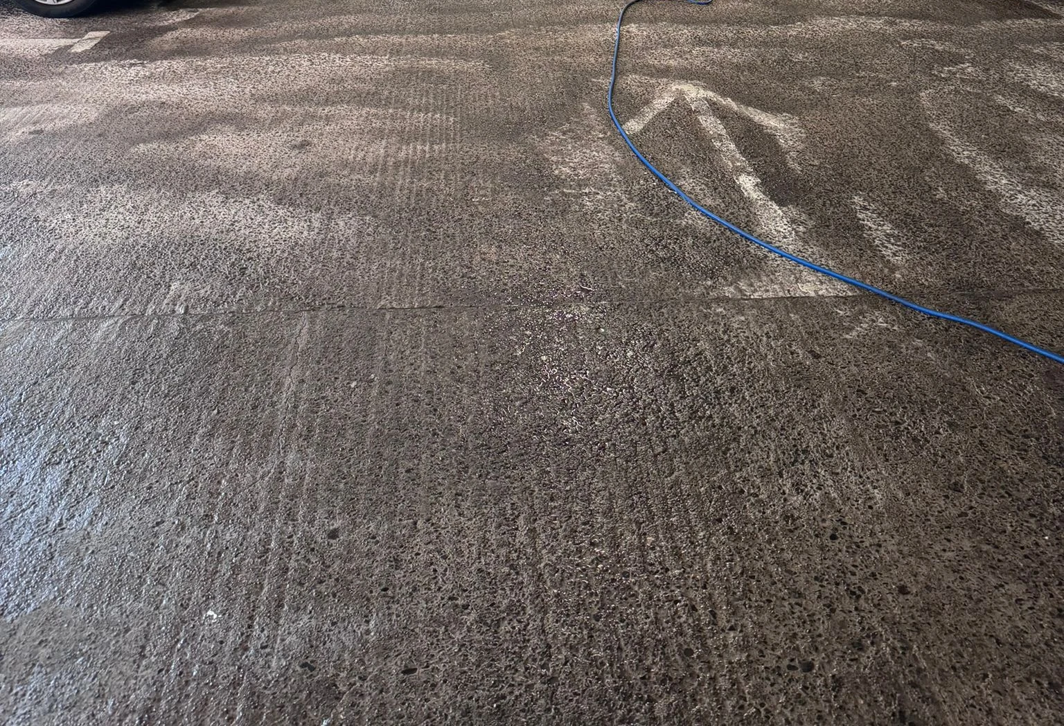 Concrete car park floor and cleaning hose during jet washing