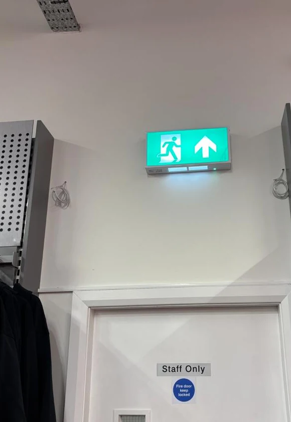 Illuminated emergency exit sign above a staff door at the Dalton Park shop
