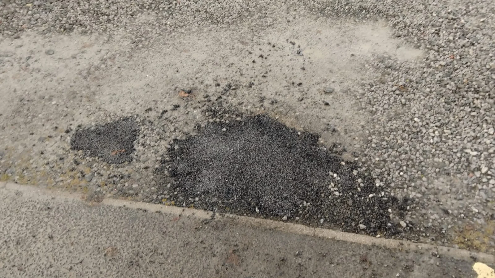 Dark compacted macadam patch within an existing tarmac car park